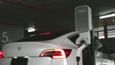 Şehir merkezindeki kapalı otoparkta yavaş çekimde EV elektrikli araba şarj oluyor. Şehir merkezinde sürdürülebilirlik yeşili, yeniden şarj edilebilir elektrikli araç iç organları.
