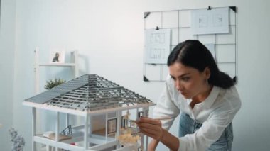 Genç, güzel ve zeki mühendisin yakın çekimleri modern ofiste duvarında taslak olan kalem kullanarak ev modelini ölçmeye odaklanıyor. Yaratıcı yaşam ve tasarım konsepti. Tertemiz..