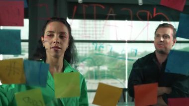 Profesyonel iş adamları yaratıcı pazarlama fikrini modern ofiste tartışırlar. İş adamları cam tahtada yapışkan notlar kullanarak finansal plan üzerinde çalışıyor. Yönlendirici.