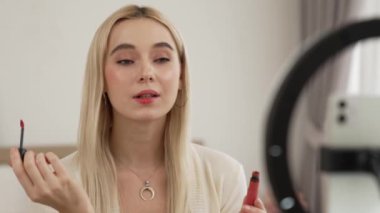 Sosyal medya için güzellik ve kozmetik video içeriği hazırlayan genç bir kadın. Seyirciye veya takipçiye nasıl sıvı ruj sürüleceğini gösterirken kamera ve ışık halkası kullanan bir güzellik blogcusu. Blithe