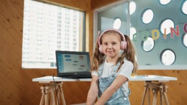 Bilgisayarda kodlama ekranı gösterilirken beyaz tatlı bir kız kameraya gülümsüyor. BTMM eğitimi almak için dizüstü bilgisayar kullanan ve kulaklık takan zeki bir çocuk. Yaratıcı. Etkinlik.