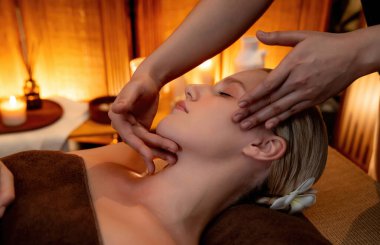 Beyaz kadın stres önleyici kafa masajı yapmaktan ve lüks otel veya otelde sıcak mum ışığında yüz güzelliği eğlencesi yapmaktan zevk alıyor. Sessiz.