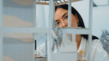 Ev modeli yapısını kendinden emin bir şekilde kontrol etmeye odaklanan genç, güzel, beyaz, yetenekli mimar mühendisinin yakın çekimi. Yaratıcı ve profesyonel tasarım konsepti. Portre. Tertemiz..