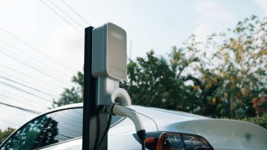 Doğal yeşil şehir parkındaki otoparkta EV elektrikli araba şarj pili. Sürdürülebilir ve çevre dostu şehir yolculuğu için yenilenebilir otomobil için alternatif temiz enerji teknolojisi. Eşzamanlama