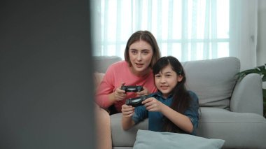 Annem kanepede yatarken, mutlu kız oyun oynuyor ve oturuyor. Beyaz bir ebeveyn ve çekici zeki bir kız elinde joystick ile birlikte vakit geçirip maç kazanmaya odaklanıyor. Yaşam tarzı. Pedagoji.