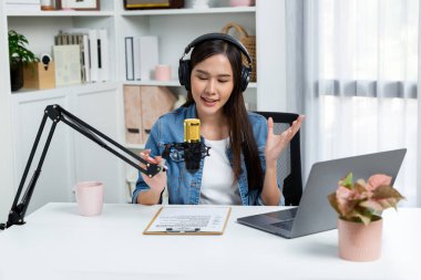 Sosyal medyada kulaklıkla canlı yayın yapan Asyalı sunucu modern stüdyoda yaşam koçluğu veya pazarlama dinleyicilerini selamlıyor. Taktik.