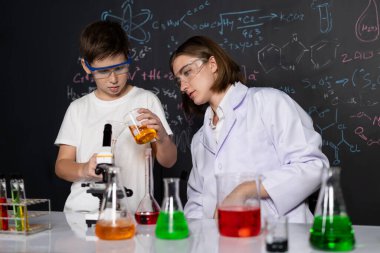 Öğretmen, laboratuarda öğrenciyi destekliyor. Öğrenci ve öğretmen cam kapta sıvı kullanarak STEM sınıfında kimya bilimi üzerine deney yapıyorlar. Karıştırma çözeltisi. Etkinlik.