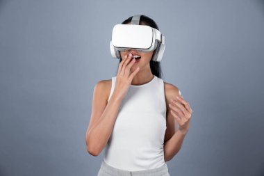 Gri arka planı olan zeki bir kadın metaevrene bağlı VR kulaklık takıyor, gelecekçi siber uzay topluluğu teknolojisi. Zarif bir kadın sanal bir manzara gördüğü için heyecanlı. Halüsinasyon.