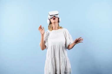 Kız çiçeğin kokusunu alırken mavi arka planda sanal gerçeklik gözlüğü takıyor. VR gözlüklü mutlu kadın görsel gerçeklik dünyasıyla bağlantı kurarken doğa hologramının keyfini çıkar. Teknoloji yeniliği. Kısıtlanma.