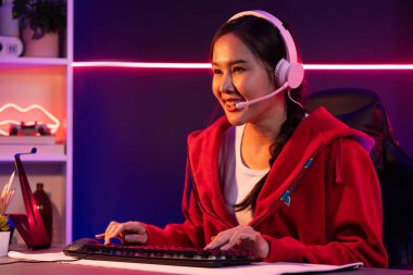 İnternet üzerinden kulaklık takıp gülümseyen Asyalı güzel kız flamasının sunucu kanalı izleyicilerle internet üzerinden konuşma yapıyor. Esport yetenekli takım oyuncuları neon mavi odada. Taktik.