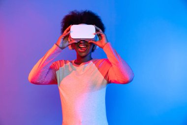 Profil, VR gözlük takan genç ve güzel Afrikalıların mavi ve pembe neon ışıklı arkaplanda izole olduğunu düşünüyor. Teknoloji ve dijital yenilik 3 boyutlu hologram gramında. Entrika.
