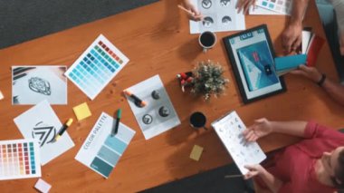 Proje yöneticisi renk paletleri seçerken tasarımcının tablete baktığı yukarıdan aşağıya hava görüntüsü. Profesyonel grafik tasarımının en üst görüntüsü ve logoya bakın. Yetenekli ekip grafikleri seçiyor. Sempozyum.