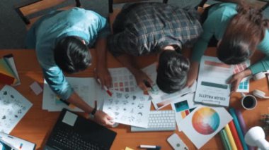 Tasarımcı fikirleri yazarken proje yöneticisinin yukarıdan aşağıya bakan görüntüsü. Akıllı iş adamları logo tasarımı fikrini açıklarken tasarımcılar palete bakarken temayı seçiyorlar. Sempozyum.