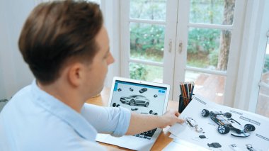 Araba tasarım mühendisi otomobil işi için otomobil prototipini ev ofisinde analiz ediyor. Otomotiv mühendisliği tasarımcısı dikkatle analiz ederek, dizüstü bilgisayarla araba tasarımında kusurlar ve iyileştirmeler buluyor.