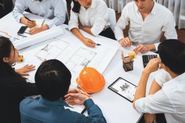 Mimari proje üzerinde birlikte çalışan çeşitli inşaat mühendisi ve müvekkil grupları, toplantı masasında tablet kullanarak inşaat planını gözden geçirip bina planı hazırlıyorlar. Tedbirli