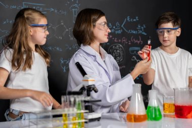 Laboratuvarda çalışan öğretmen, güvenlik gözlüğü takıyor, STEM sınıfında kimya bilimi üzerine deney yapıyor. Öğrenci komedisi tüpte sıvı deneyi yapar. Etkinlik.