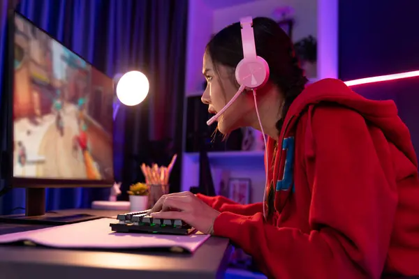 stock image Host channel of young beautiful Asian gaming streamer, playing battle team gaming with multiplayer or single at warship on screen, wearing pastel color headset at digital neon light room. Stratagem.