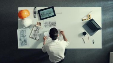 Proje planını kontrol ederken ve seçerken mimar mühendisin bina planlarını masaya yerleştirdiği tepeden aşağı hava görüntüsü. İç mimar toplantı masasından mimari plan seçti. Hizalama.