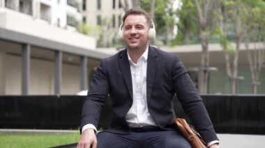 İş adamları yeşil şehirde şarkıya taşınırken dinlenmek için kulaklık takarlar. Motivasyonlu kulaklık kullanırken neşeli bir şekilde dans eden mutlu proje yöneticisi hareketi. Urbane.