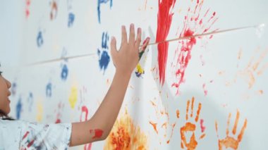 Resim sınıfındaki öğrenci tarafından renkli lekeli duvarın kapağı boyandı. Dağınık odada renkli suluboyalarla oynayan komik Asyalı kız. Yaratıcı aktivite konsepti. Etkinlik.