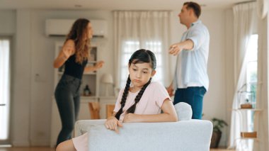 Sinirli ve mutsuz genç bir kız oturma odasında ebeveyninin tartışması yüzünden gerginliğin ortasında kanepede oturuyor. Sağlıksız ev hayatı ve travmatik çocukluk depresyon senkronlarına dönüşür.