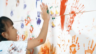 Resim sınıfındaki öğrenci tarafından renkli lekeli duvarın kapağı boyandı. Dağınık odada renkli suluboyalarla oynayan komik Asyalı kız. Yaratıcı aktivite konsepti. Etkinlik.