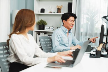 Gülümseyen Asyalı bir adam, yan görüntüdeki modern ofis çalışma masasında veri tabanını ararken günlük dizüstü bilgisayarla pazarlama raporu projesini planlarken kadın meslektaşıyla konuşuyor. İnfobahn.