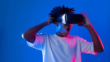 Sanal gerçekliği dijital fütüristik teknolojiye bağlayan pembe mavi neon duvarda VR 'dan bakan genç Afrikalı Amerikalı' ya şaşırdım. Entrika.