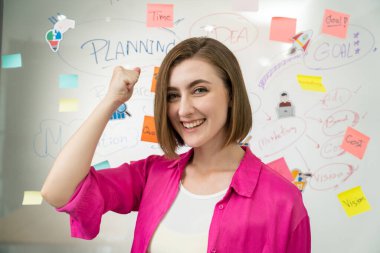 Beyaz tahtanın önündeki kameraya zihin haritası ve renkli yapışkan notlarla bakarken gülümseyen ve kendinden emin bir şekilde poz veren genç beyaz iş kadınının portresi. - Yakın çekim. Tertemiz..