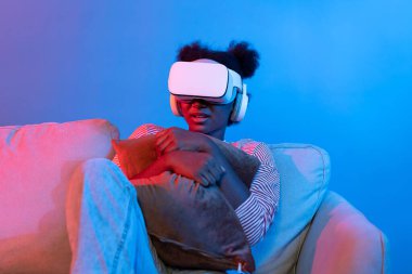 Genç Afrikalı, VR gözlükleriyle korku filmi seyrediyor. Fantastik 3D korku filmi fütüristik teknolojide korkuyor. Sanal gerçeklik, oturma odasındaki koltukta metatif seyahat dünyası. Entrika.