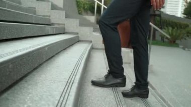 Yakından bakınca iş için çanta tutarken yürüyen zeki bir iş adamının görüntüsü var. Proje yöneticisi çalışmak için merdivenlerden iniyor. Ulaşımı temsil eden, seyahat eden. Bacağa odaklan. Sevinçli..