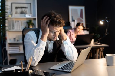 Ciddi yüzü olan bir adam modern ofiste gece aydınlatma zamanı yaratıcı proje planlaması yapıyor bulanık sekreterle birlikte klasör arkaplan konseptiyle kağıt raporlarını kontrol ediyor. Varsayım.