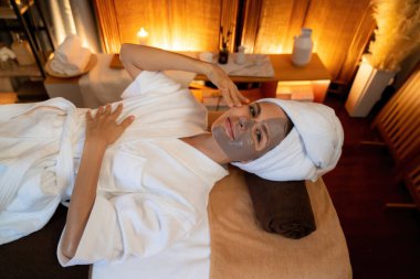 Kaplıca salonunun sakin atmosferi, üst düzey kadın müşteri sıcak mum ışığında kömür kömürü yüz kremi masajıyla kendini yenilemeye çalışıyor. Yüz bakımı ve güzellik konsepti. Sessiz.