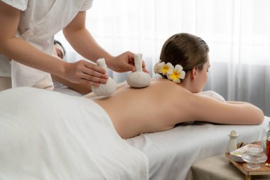 Sıcak bitkisel top spa masaj vücut tedavisi, masör nazikçe bitki torbasını çift müşteri vücuduna bastırıyor. Aromaterapi dinlenme sükuneti ve sükuneti kaplıca salonundaki atmosferi aydınlatıyor. Sessiz.