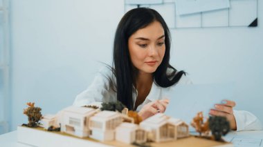 Genç ve güzel mimarın yakın plan çalışması, mimari modelle ev modeli ve toplantı odasındaki masanın üzerine yerleştirilen mimari ekipmanları karşılaştırıyor. Yaratıcı tasarım konsepti. Tertemiz..