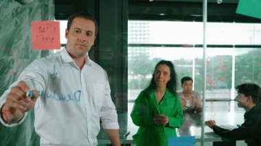 Yetenekli işadamı, cam duvara renkli yapışkan notlar yapıştırarak proje yöneticisine pazarlama fikrini sundu. Proje yöneticisi yatırımcıya projeyi gösteriyor, anlatıyor, gösteriyor. Yönlendirici.