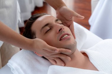 Beyaz adam stres önleyici kafa masajından ve lüks bir tatil beldesi veya otel spa salonundaki modern ışık ortamında yüz güzelliği eğlencelerini şımartmaktan hoşlanıyor. Sessiz.