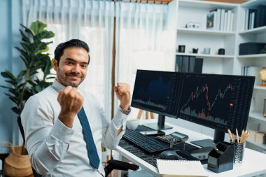 Tüccar işadamının iki borsa yatırım ekranı ile kameraya bakması, yüksek kar elde etmek için yumruğunu kaldırması ve ofisteki dinamik finansal teknoloji grafiği borsasında başarılı olması. Tahmin et..