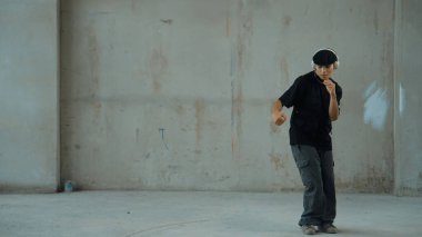 Kulaklıktan çimento arka planda müzik dinlerken break dans pratiği yapan yakışıklı bir hippi. Sokak dansçısının hareketli çekimi robot dansı yapar. Açık hava sporu 2024. Modern dans. hiphop.