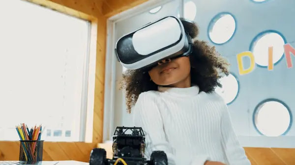 stock image Creative girl wearing VR headset to learning in metaverse. Funny kid enjoy to wearing AI headset and enter to virtual world program in STEM technology class. Innovation. Future lifestyle. Erudition.