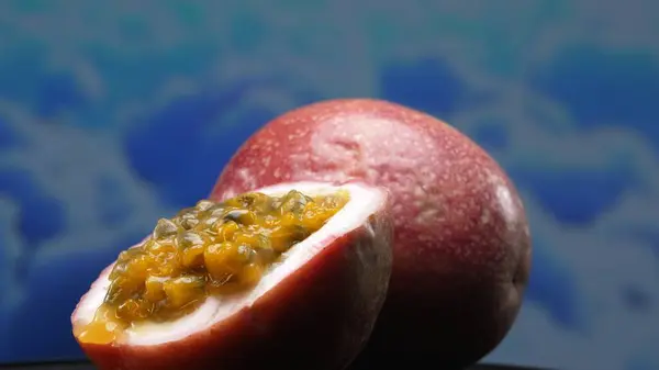 stock image A halved passion fruit, bursting with jewel tones, rests upon a calming, blue background. The juicy flesh, a tangy-sweet treasure trove, is filled with pulp and black seeds. Close up. Comestible.