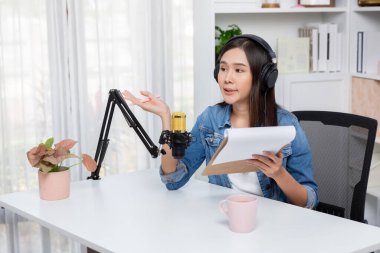 Sosyal medyada kulaklıkla canlı yayın yapan Asyalı sunucu modern stüdyoda yaşam koçluğu veya pazarlama dinleyicilerini selamlıyor. Taktik.