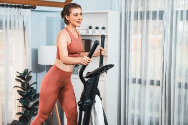 Spor ve atletik bir kadın, evdeki fiziğe ve sağlıklı spor yaşam tarzına uygun vücut egzersizi sırasında eliptik koşu makinesiyle koşuyor. Gaiety evde egzersiz eğitimi.