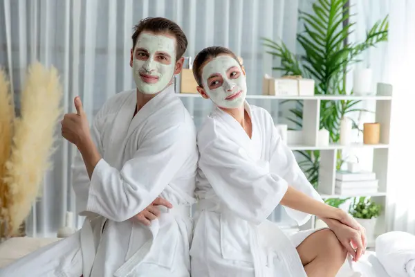 stock image Blissful couple in bathrobe with facial cream mask enjoying serene ambiance of spa salon resort or hotel during holiday. Pampering face spa and skincare treatment with essence relaxation. Quiescent