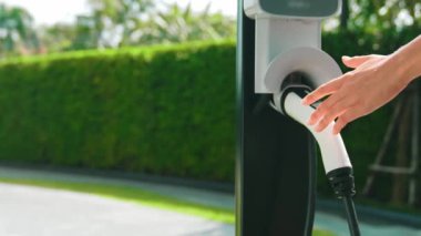 Yavaş çekim kadın, yeşil sürdürülebilir şehir parkı bahçesinde şarj olan EV elektrikli arabasıyla geziyor. Sürdürülebilir kentsel yaşam tarzında, yeniden şarj edilebilir elektrikli araç iç organlarıyla alışverişe gidiyor.