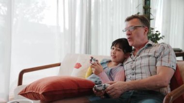 Granddaughter teaching grandfather play console game, entertainment hobby. Old senior use technology communicate with new generation kid cross generation gap strengthen family bond. Divergence.