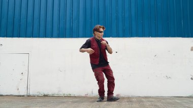 Beyaz arka planda break dans pratiği yapan yakışıklı bir sokak dansçısı. Hip hop tarzı giyinen sporcu, mavi arka planlı bir sokakta müzik eşliğinde ayak sesleri çıkarıyor. Açık hava sporu 2024 hiphop..