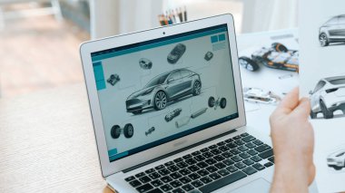 Araba tasarım mühendisi otomobil işi için otomobil prototipini ev ofisinde analiz ediyor. Otomotiv mühendisliği tasarımcısı dikkatle analiz ederek, dizüstü bilgisayarla araba tasarımında kusurlar ve iyileştirmeler buluyor.