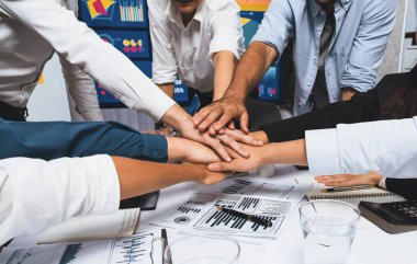 Çeşitli ofis çalışanlarından oluşan bir grup, ofis odasında el ele vererek iş sinerjisini ve iş yerindeki güçlü verimli takım çalışmasını sembolize ediyor. İş çalışanları arasındaki işbirliği ve birlik. Tedbirli