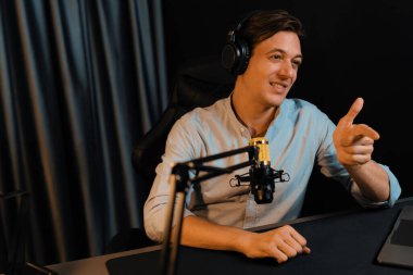 Sunucu kanalı akıllı yayıncı laptopta canlı sosyal medya uygulaması arıyor, kulaklık takıyor ve modern ofis stüdyosundaki mikrofonu kullanıyor. Bireysel.